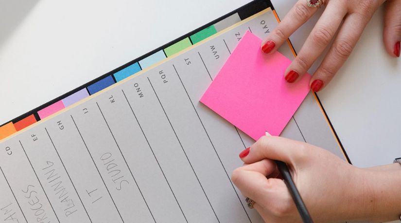 Hand writing on pink sticky note over planner