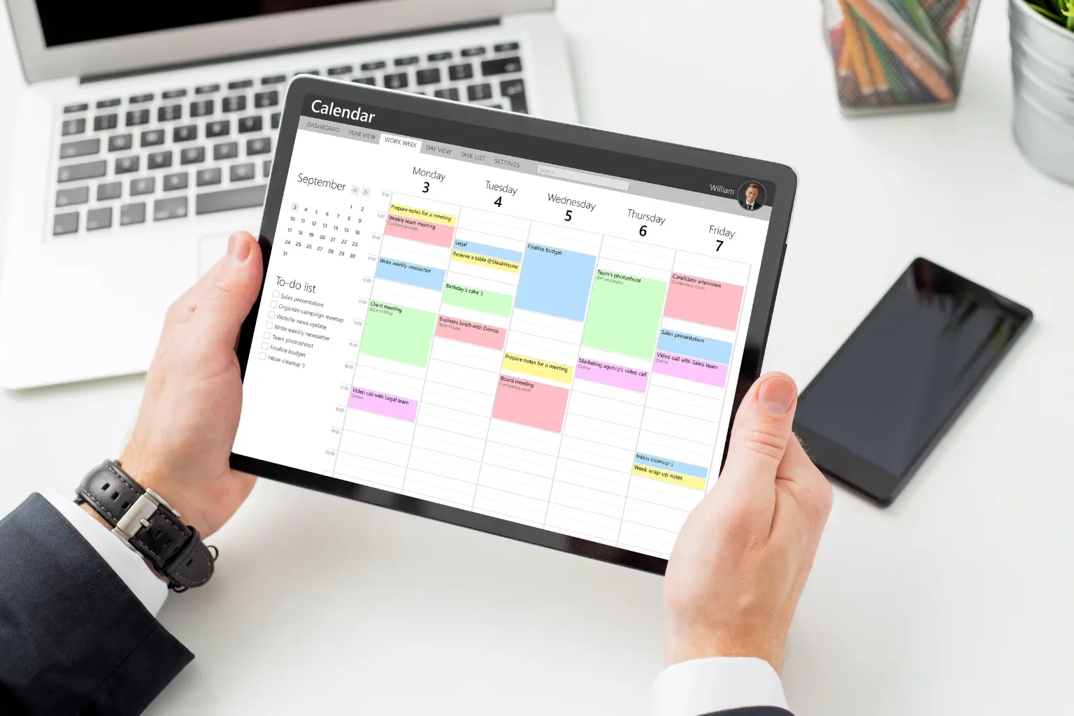 business appointment software man holding tablet showing weekly schedule grid with colorful blocks