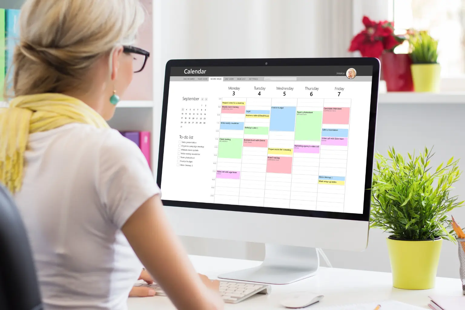 Woman viewing a color-coded calendar on desktop monitor