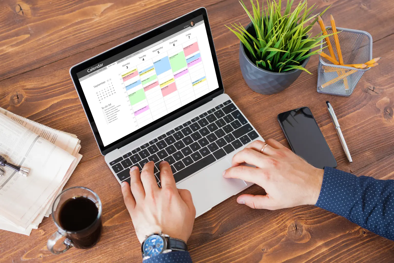 appointment scheduling software user typing on laptop showing desktop calendar interface with multi-colored events