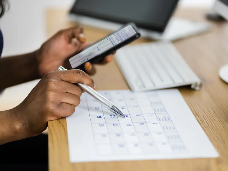 Appointment scheduling apps help organize tasks, as a person checks dates on a paper calendar while using a smartphone