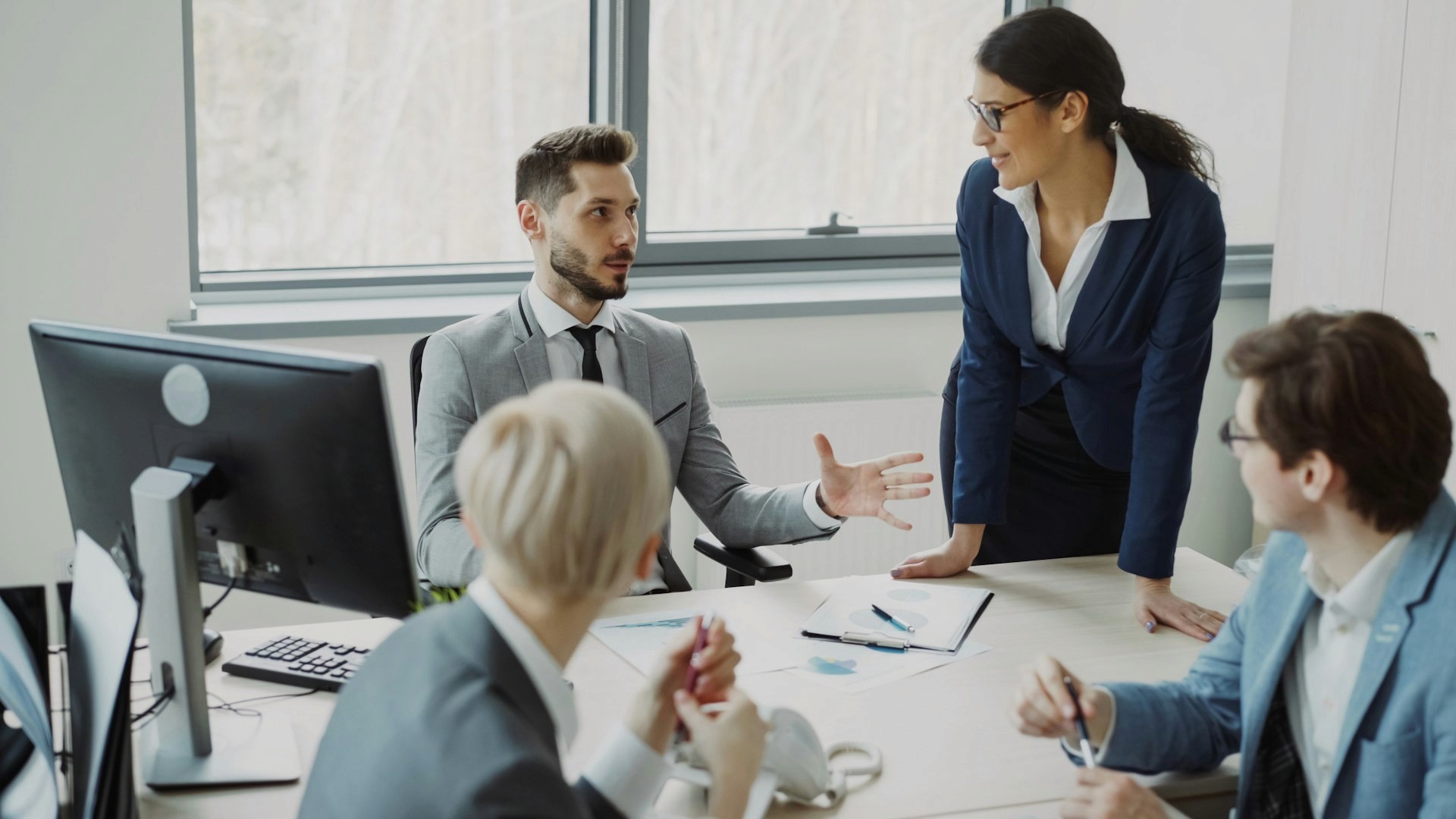Colleagues engaged in a strategy meeting, reviewing documents and discussing sales data in a bright office environment.