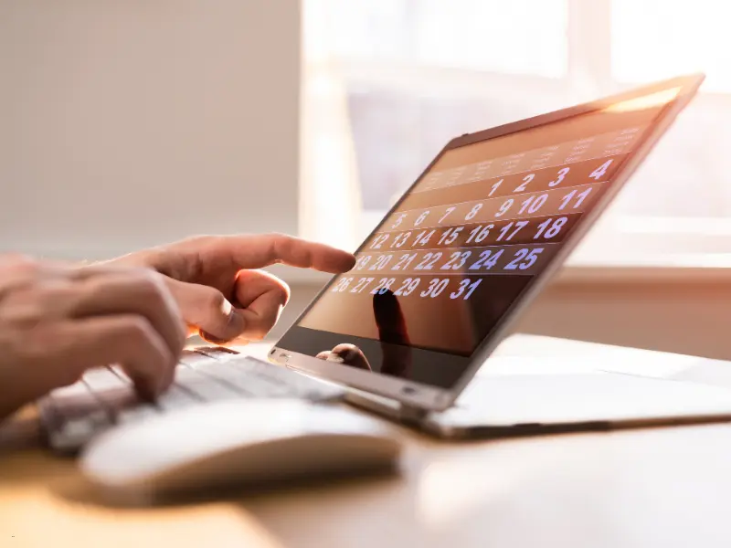 Smart calendar scheduling on a touchscreen laptop, with a person selecting a date in a sunlit workspace.
