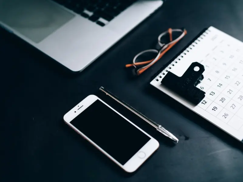Best scheduling tools include a desk setup with a calendar, smartphone, pen, glasses, and a laptop