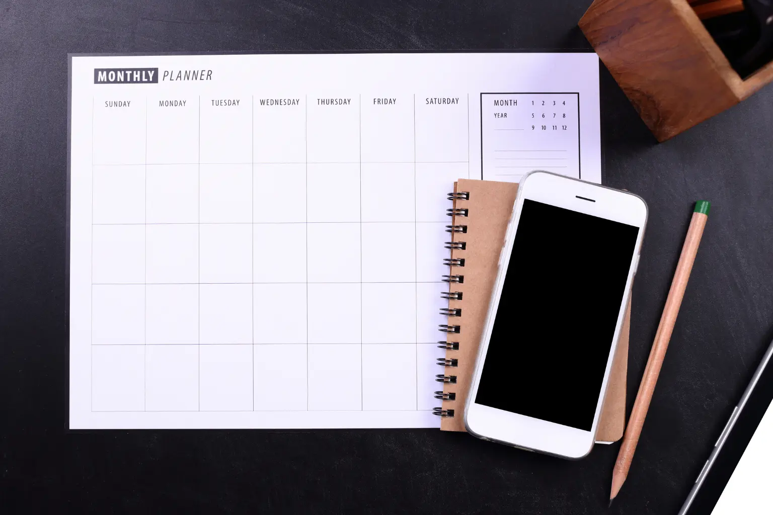 Monthly planner, notebook, and phone on desk