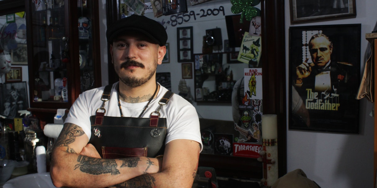Portrait of a tattooed barber with arms crossed in his shop