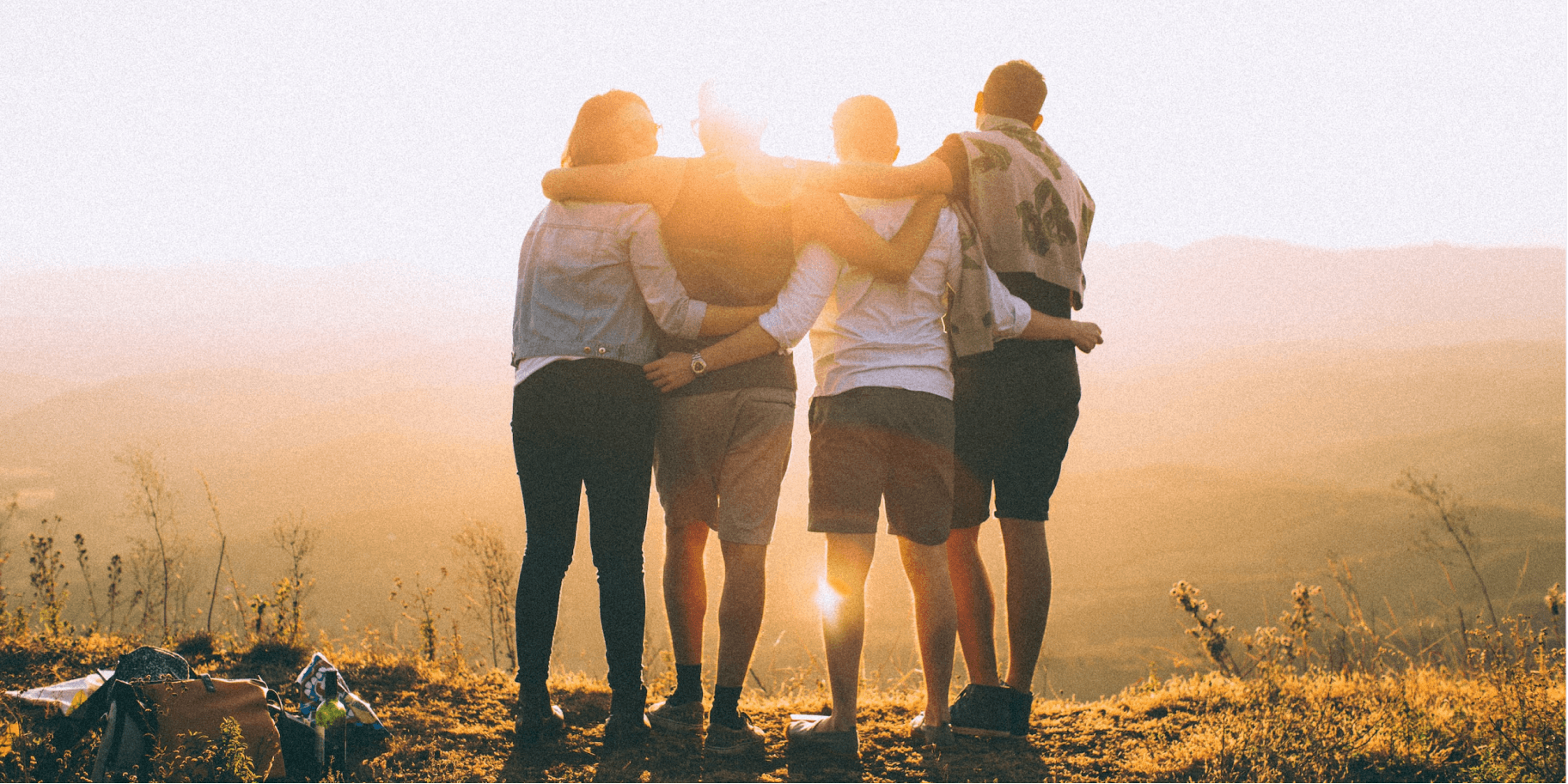 Friends embracing while watching a sunset on a hill