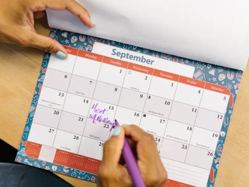 Appointment booking system in use as a person writes a meeting reminder on a colorful paper calendar