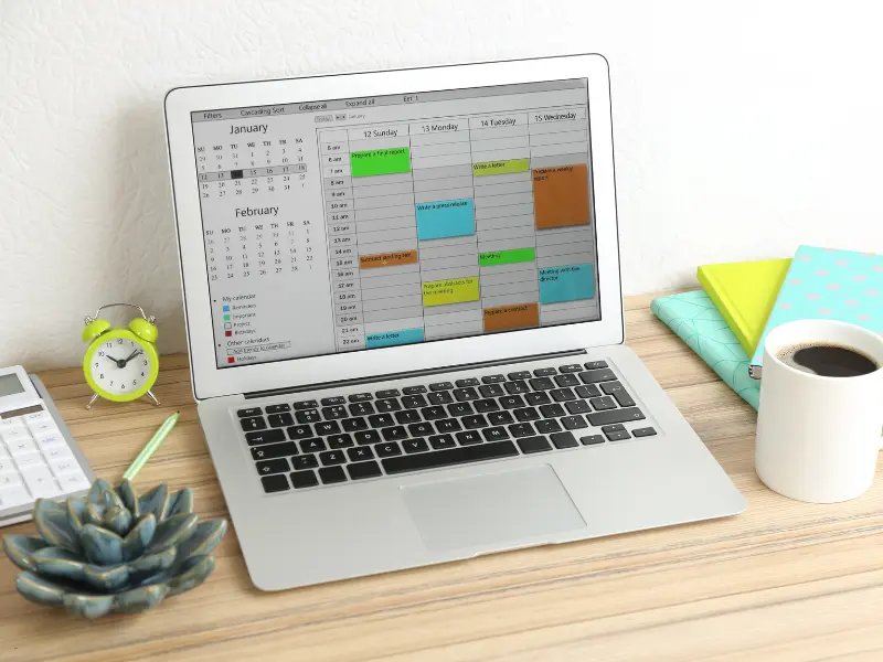 Appointment management on a laptop screen displaying a digital calendar, surrounded by office supplies and a coffee cup