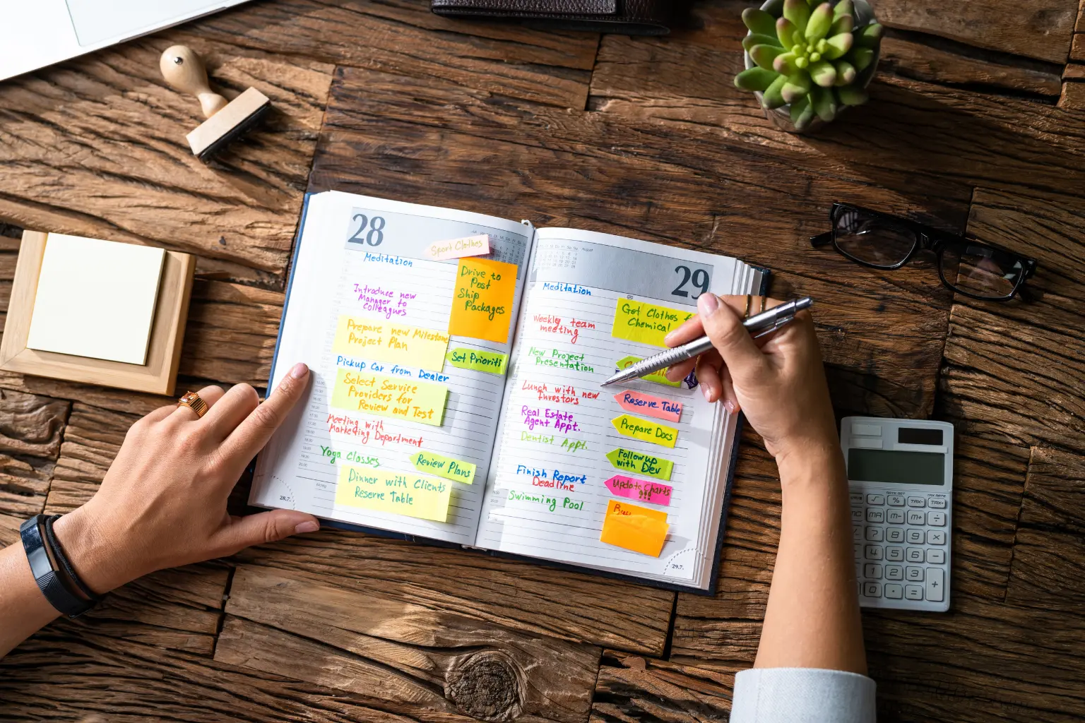 Hands writing in a planner with sticky notes on desk