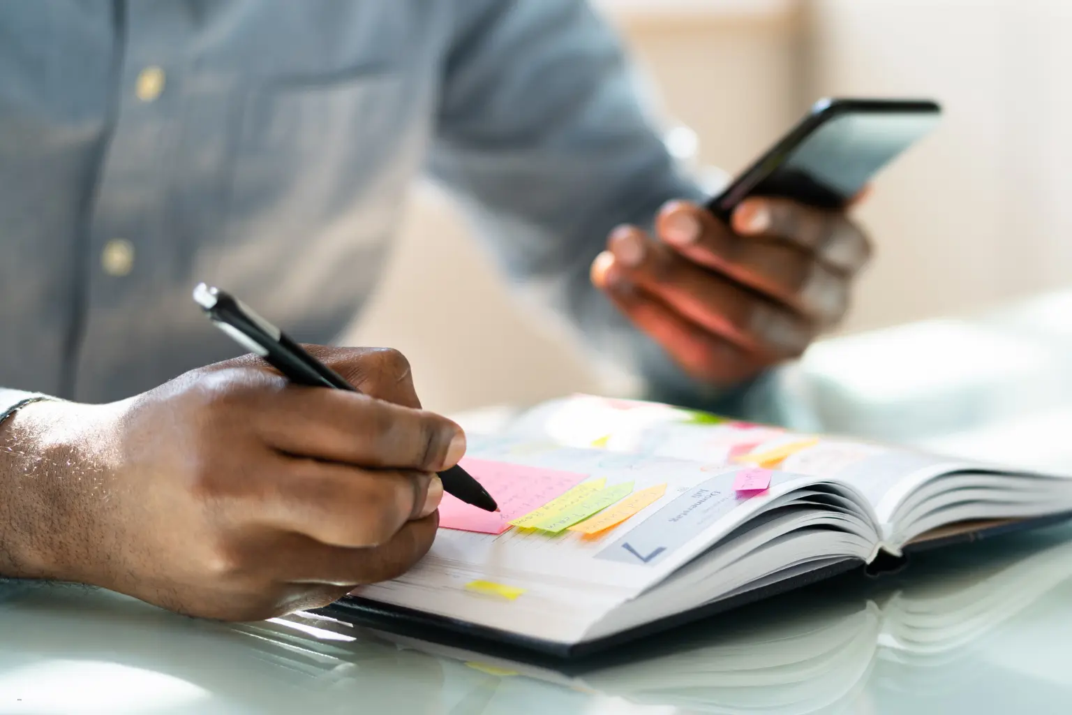 Scheduling automation for teams with a person using a smartphone and writing notes in a planner with sticky notes