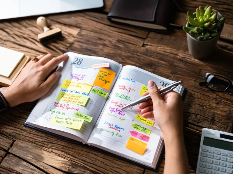 Meeting management software planning with a detailed, handwritten schedule in a daily planner.