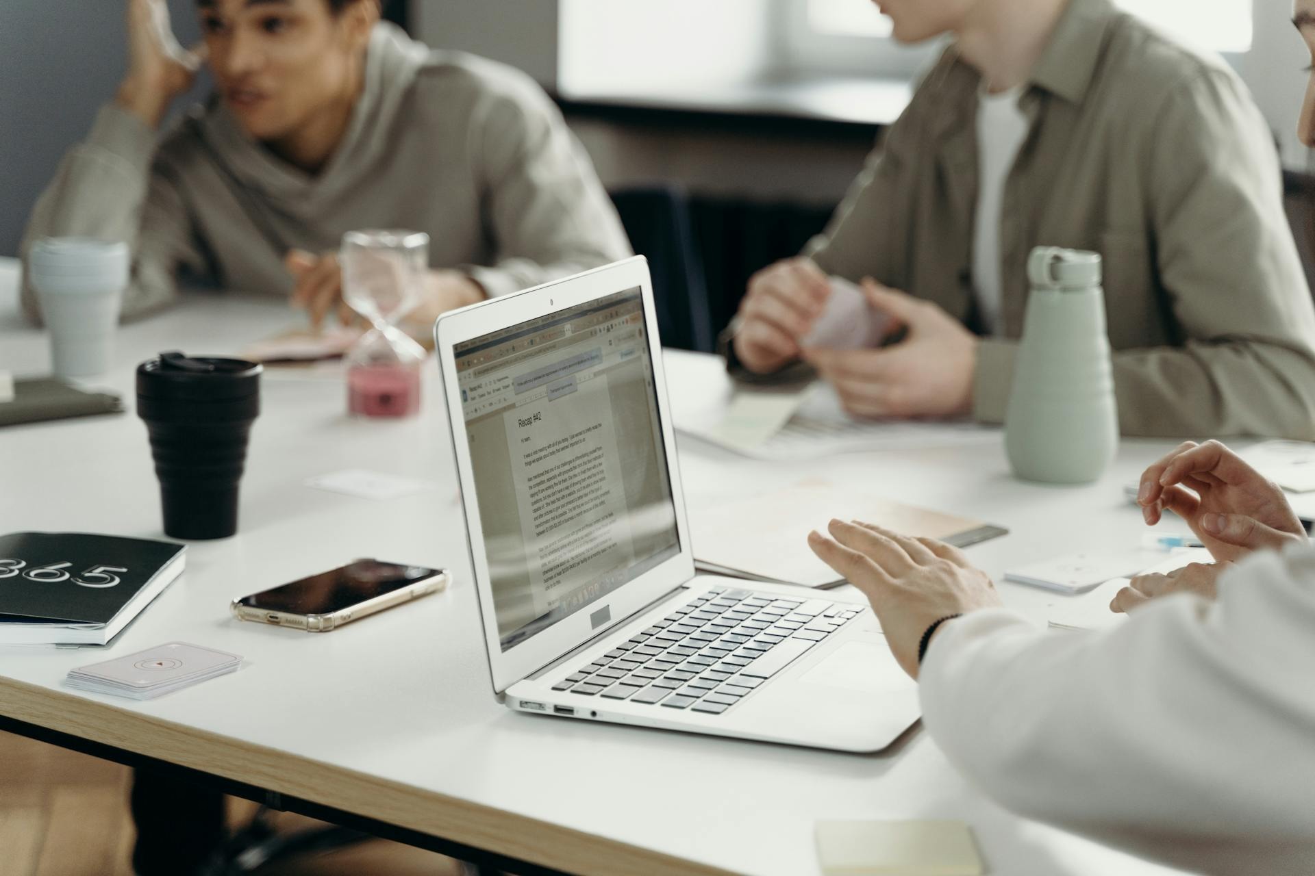 A close-up of an open laptop on a workspace table during a collaborative marketing team meeting.