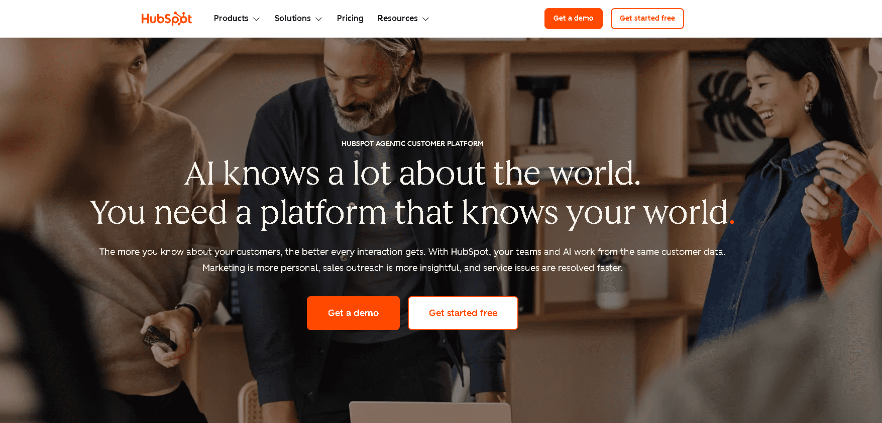 The HubSpot homepage featuring text for their Agentic Customer Platform overlaying a team collaborating around a laptop.
