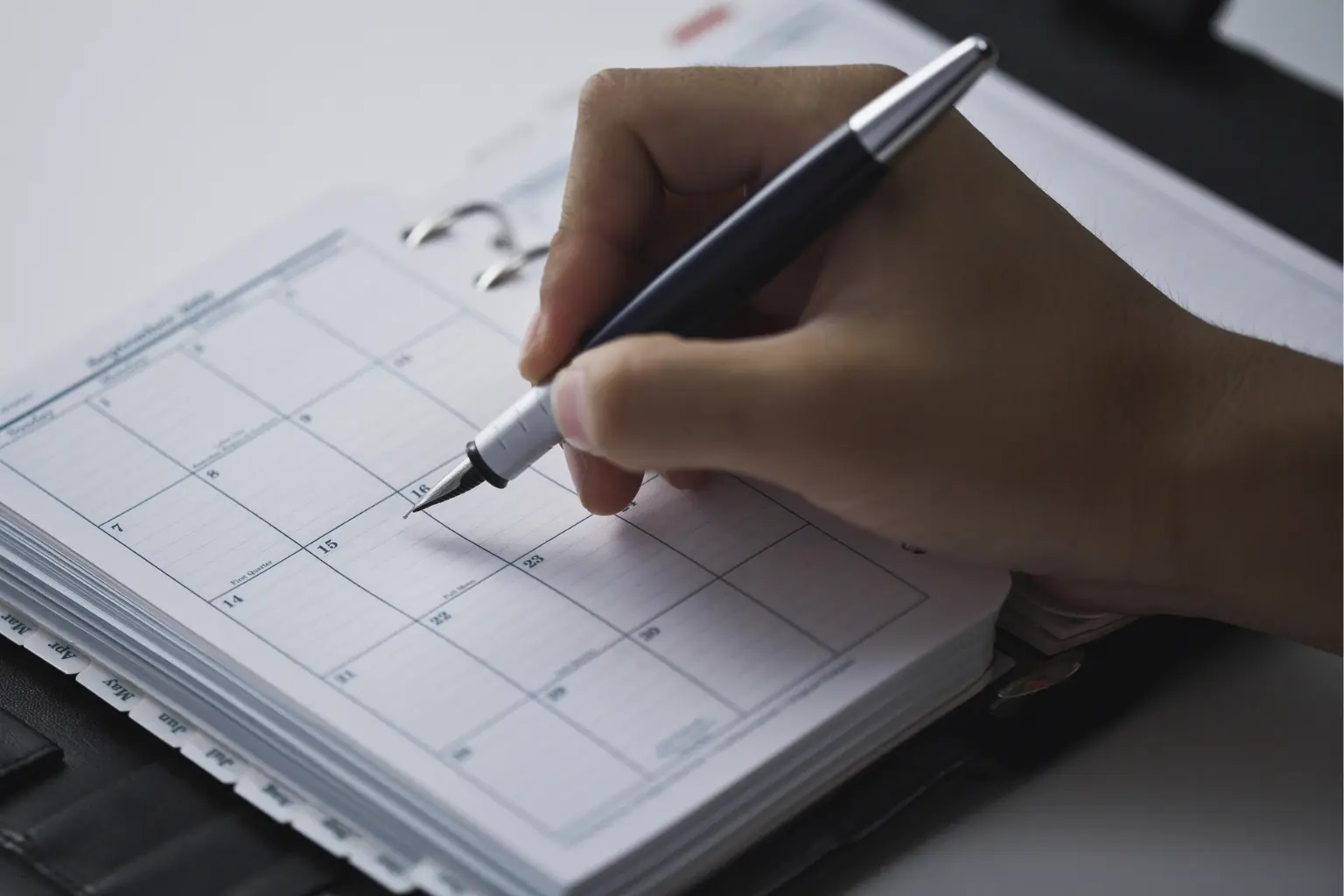Hand marking a date on a paper calendar planner