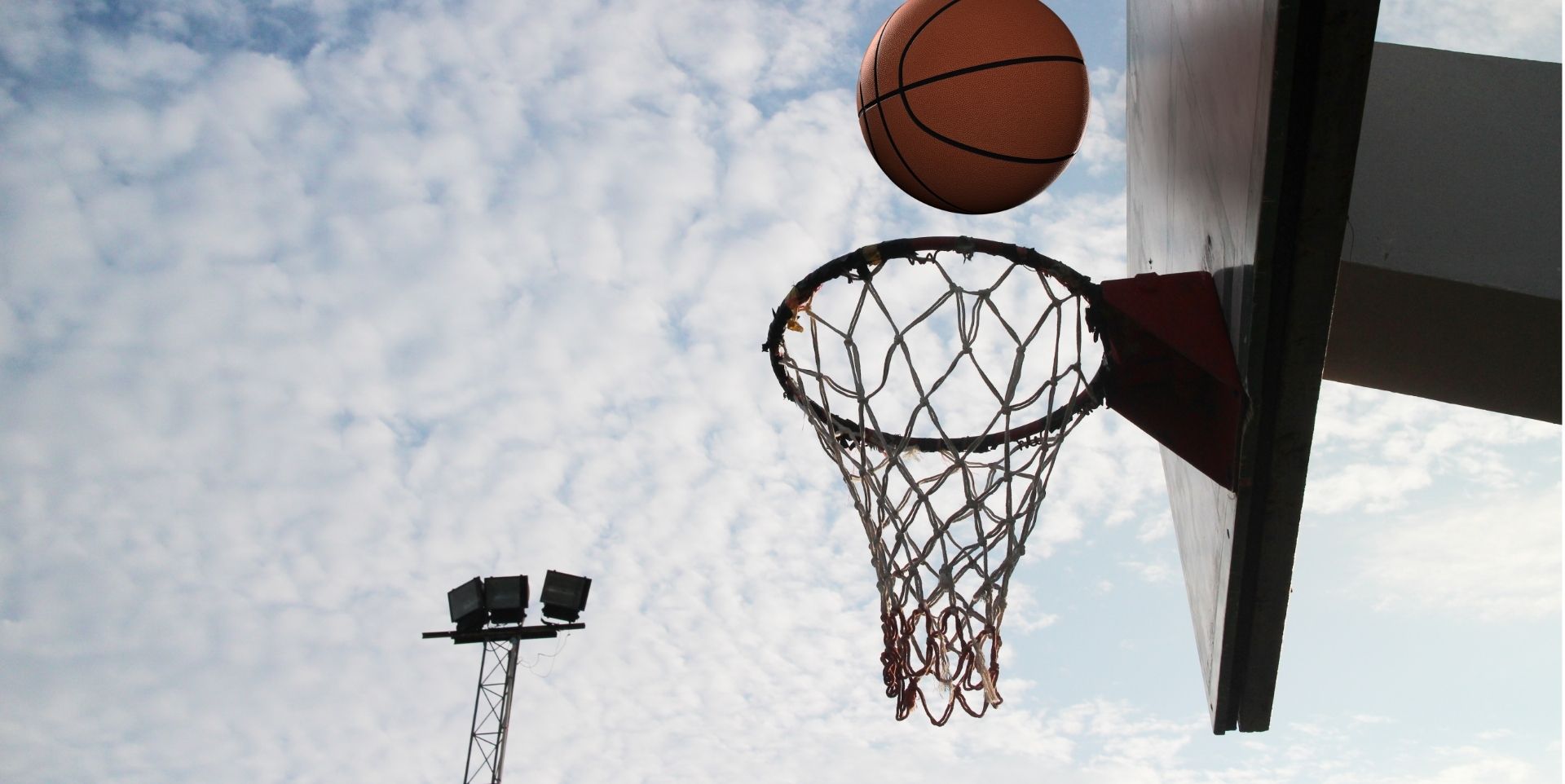 Basketball flying into hoop against a cloudy sky