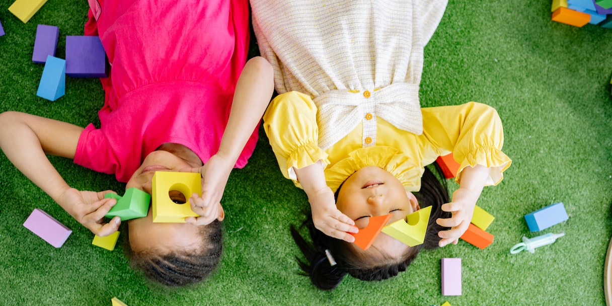 Two children playing with wooden blocks on grass
