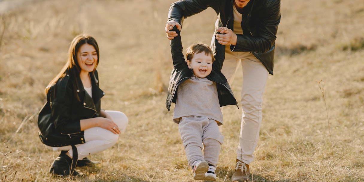 Parents swinging a laughing child in a field