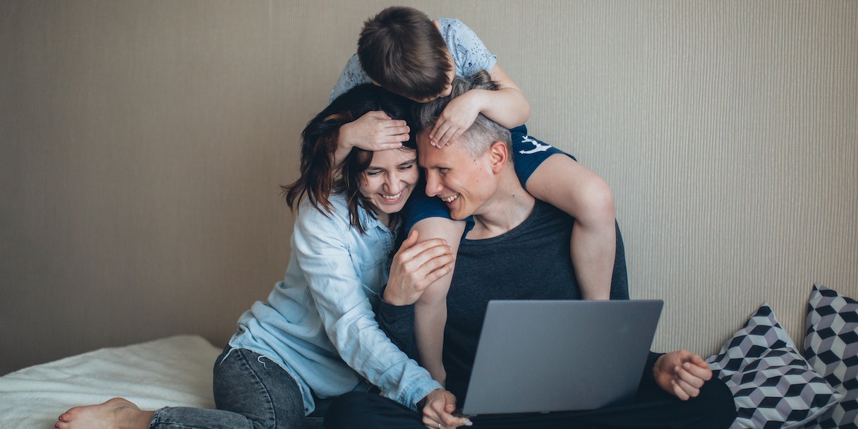 Family cuddling together with a laptop on the bed