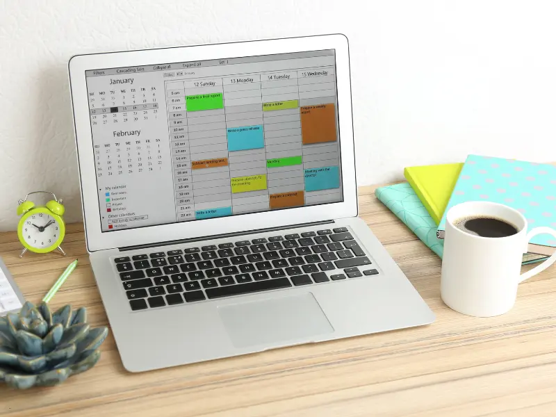Appointment scheduling software open on a laptop with a colorful weekly calendar view and personal workspace setup.