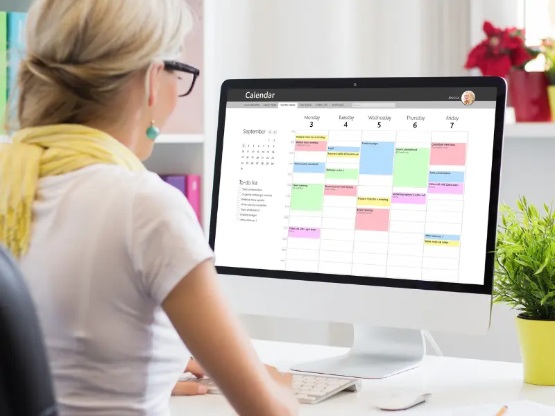 Top calendar tool on a large desktop monitor used by a woman managing her busy weekly schedule.