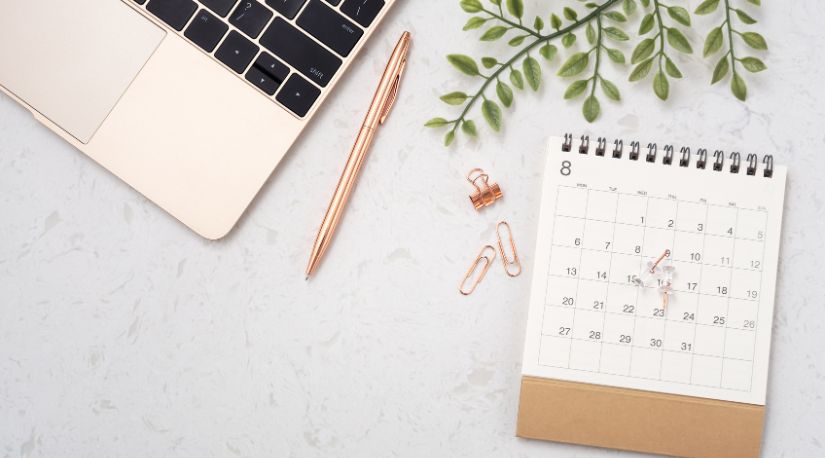 Desk calendar, pen and paper clips beside a laptop