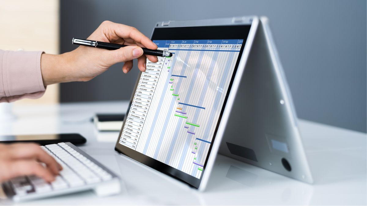 Hand pointing pen at a Gantt chart on a laptop screen