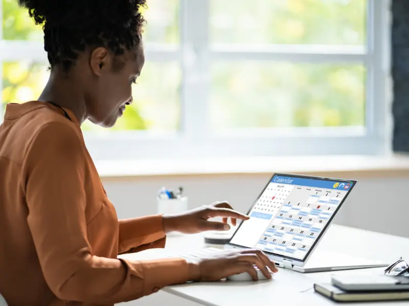 Advanced scheduling software displayed on a laptop as a woman organizes her calendar in a bright office