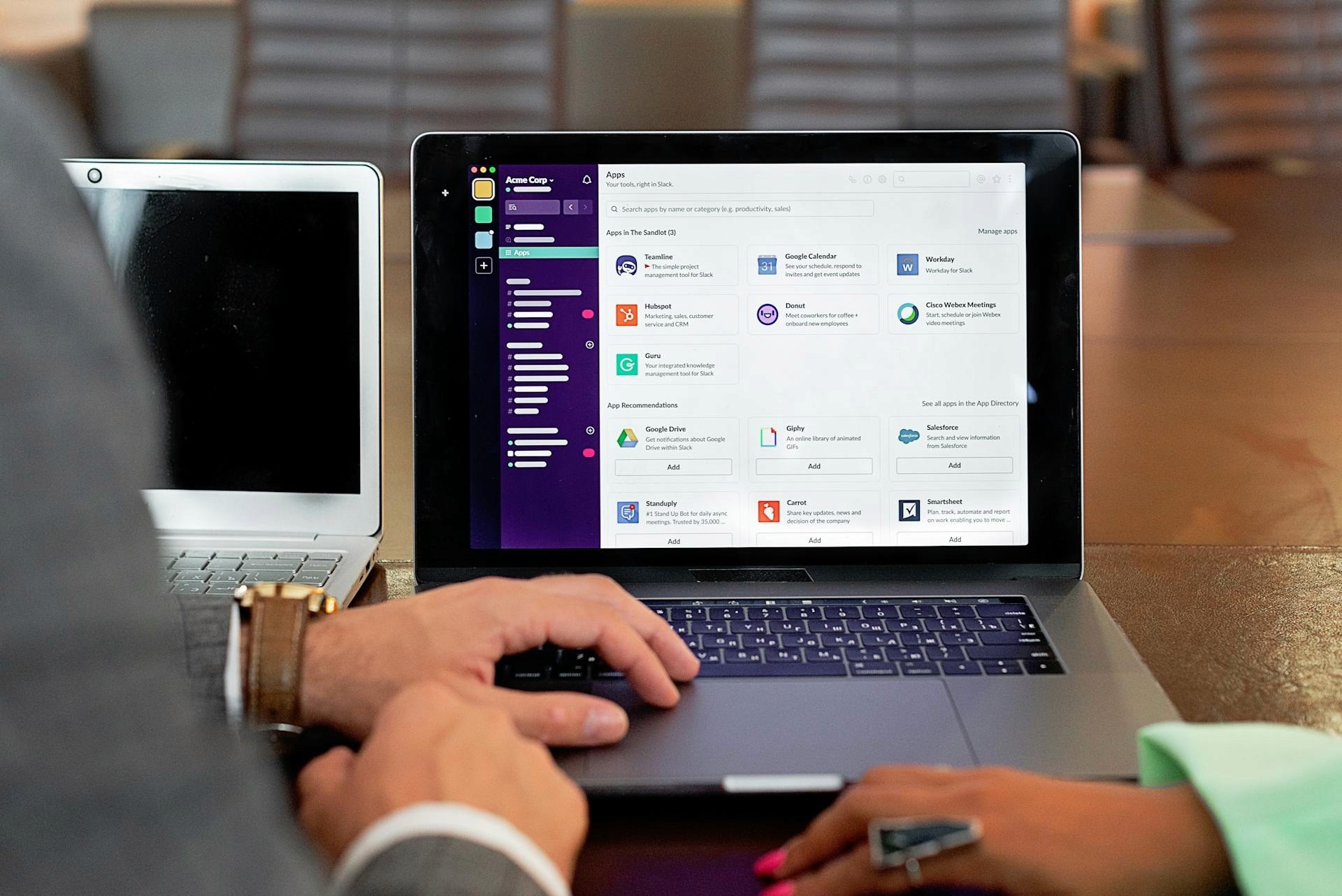 Close-up of a laptop screen displaying a professional app directory including HubSpot and Salesforce integrations, being used by two people in a business meeting setting.