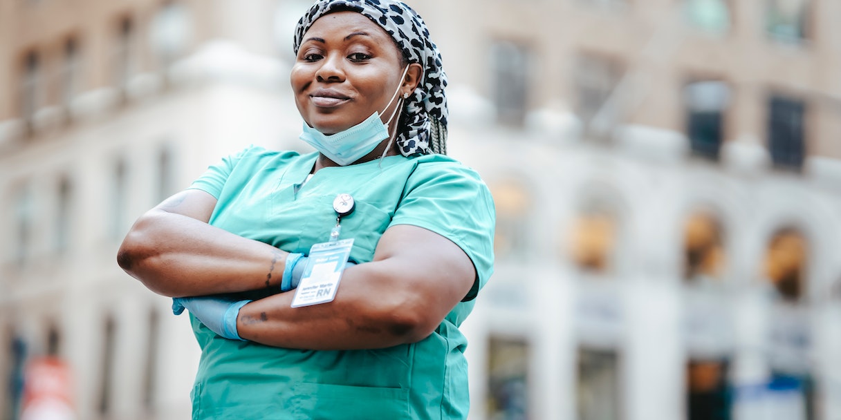 Nurse in scrubs standing with arms crossed on a city street