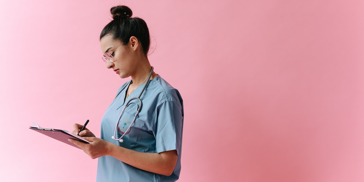 Nurse in scrubs writing on a clipboard
