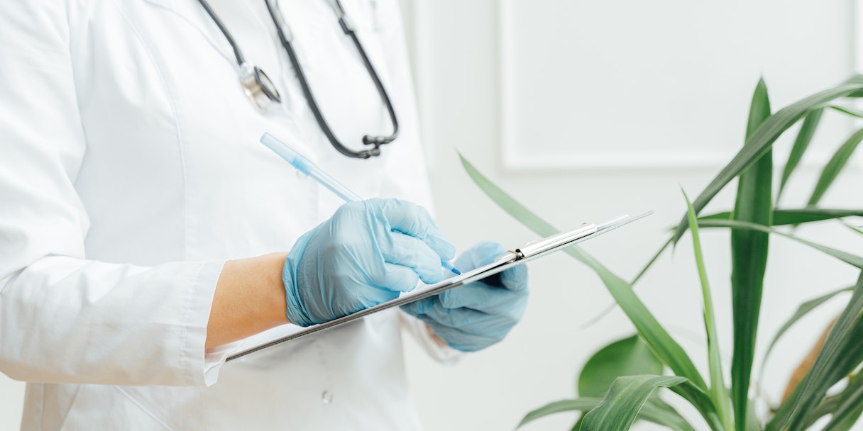 Nurse writing on a clipboard beside a plant