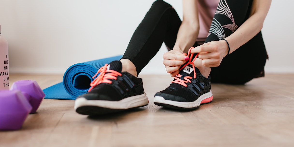 Photo of someone tying a running shoe by a yoga mat