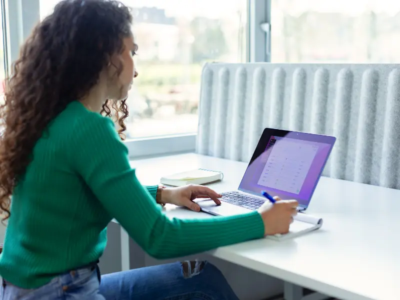 Meeting efficiency tools in use as a woman takes notes while reviewing a digital schedule on her laptop.