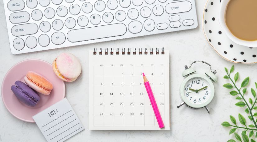 Desk flat lay with a calendar, clock, and macarons