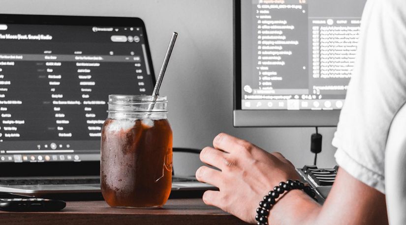 Iced coffee on desk beside dual monitors with code