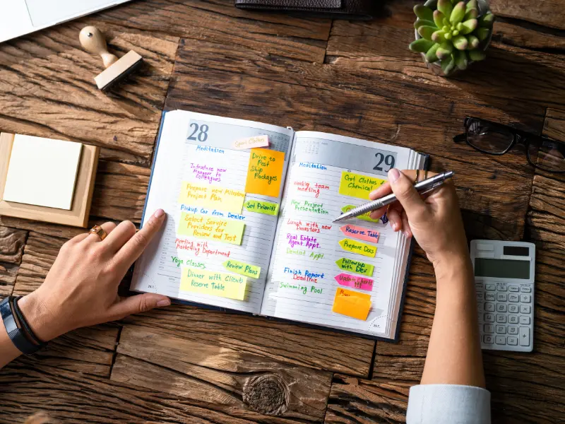 Digital time management tools used with colorful sticky notes in a detailed planner on a wooden desk