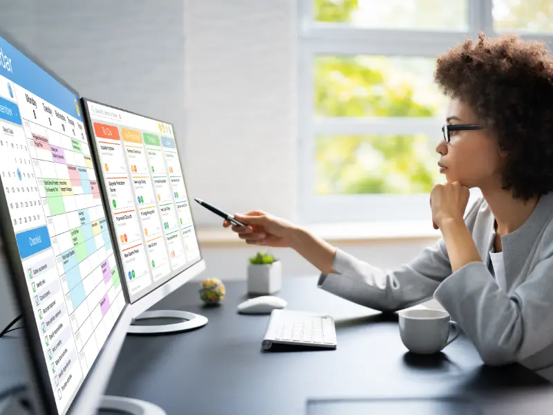Tools for managing time demonstrated by a woman using dual monitors to organize calendar and task lists