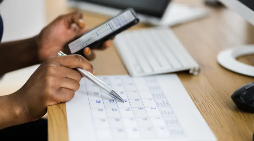 Hands marking dates on a printed calendar with a phone