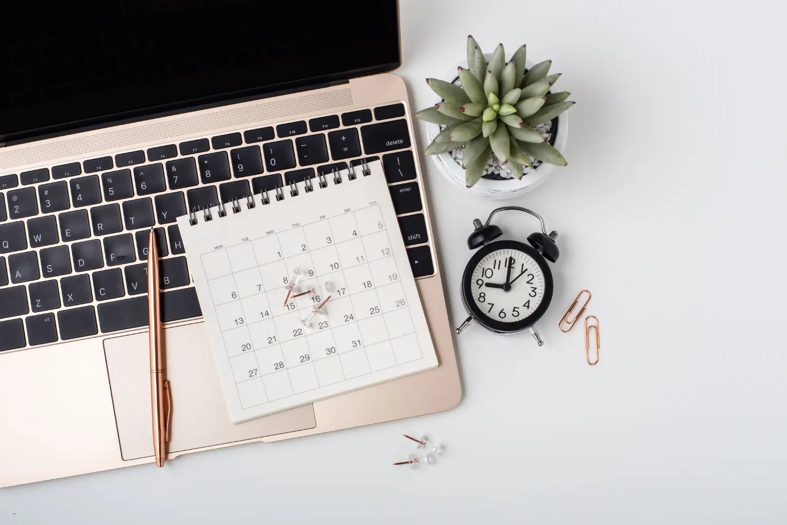 Desk calendar, alarm clock and succulent beside a laptop