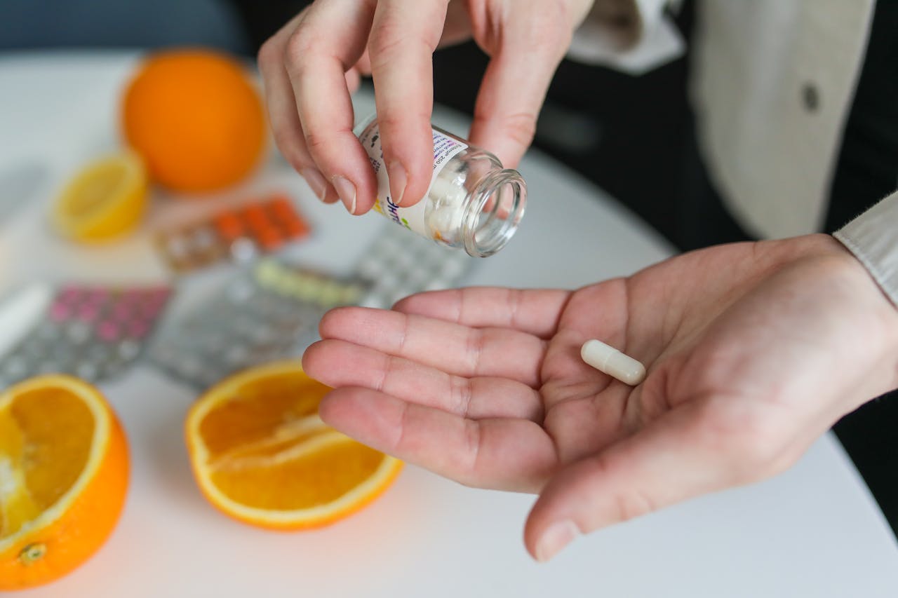 Hands holding vitamin pills near oranges