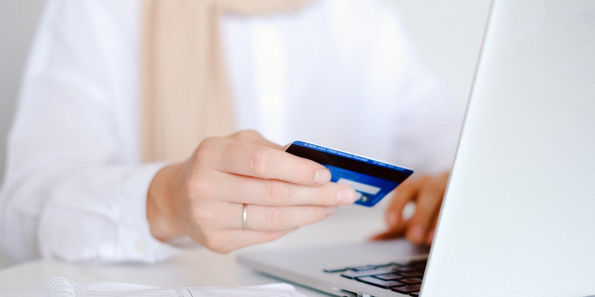 Close-up of a hand holding a credit card near a laptop