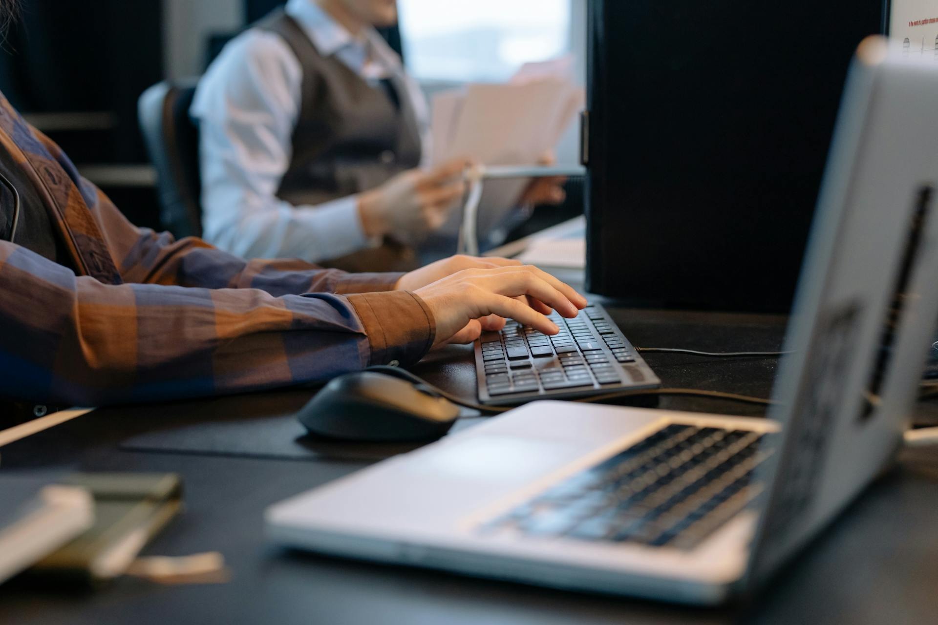 Close-up of a sales representative's hands typing on a keyboard at a desk with a laptop and computer monitor, representing efficient lead scheduling and CRM management.