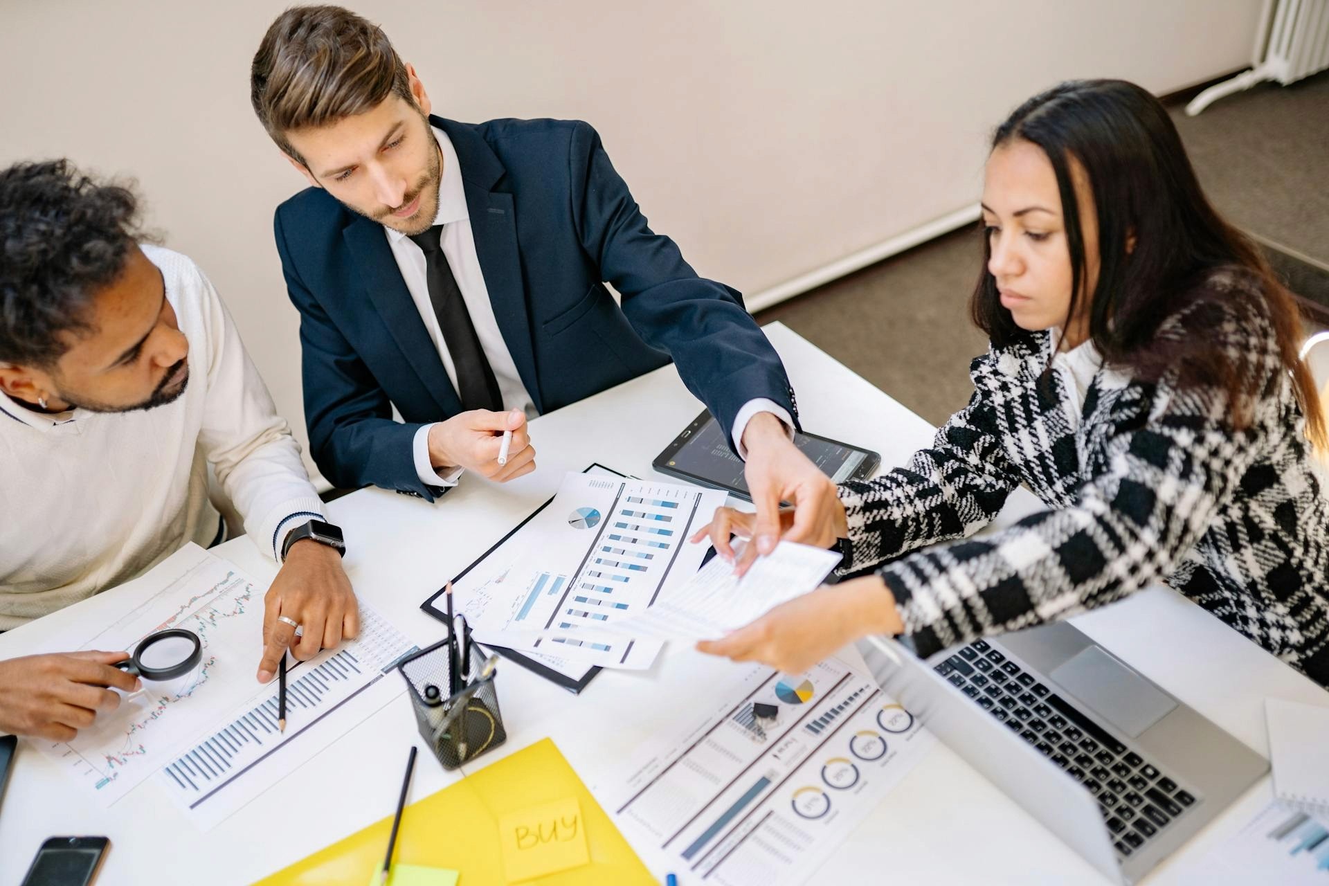 A corporate business team collaborating at a conference table, reviewing printed pipeline reports and data charts with a laptop open.