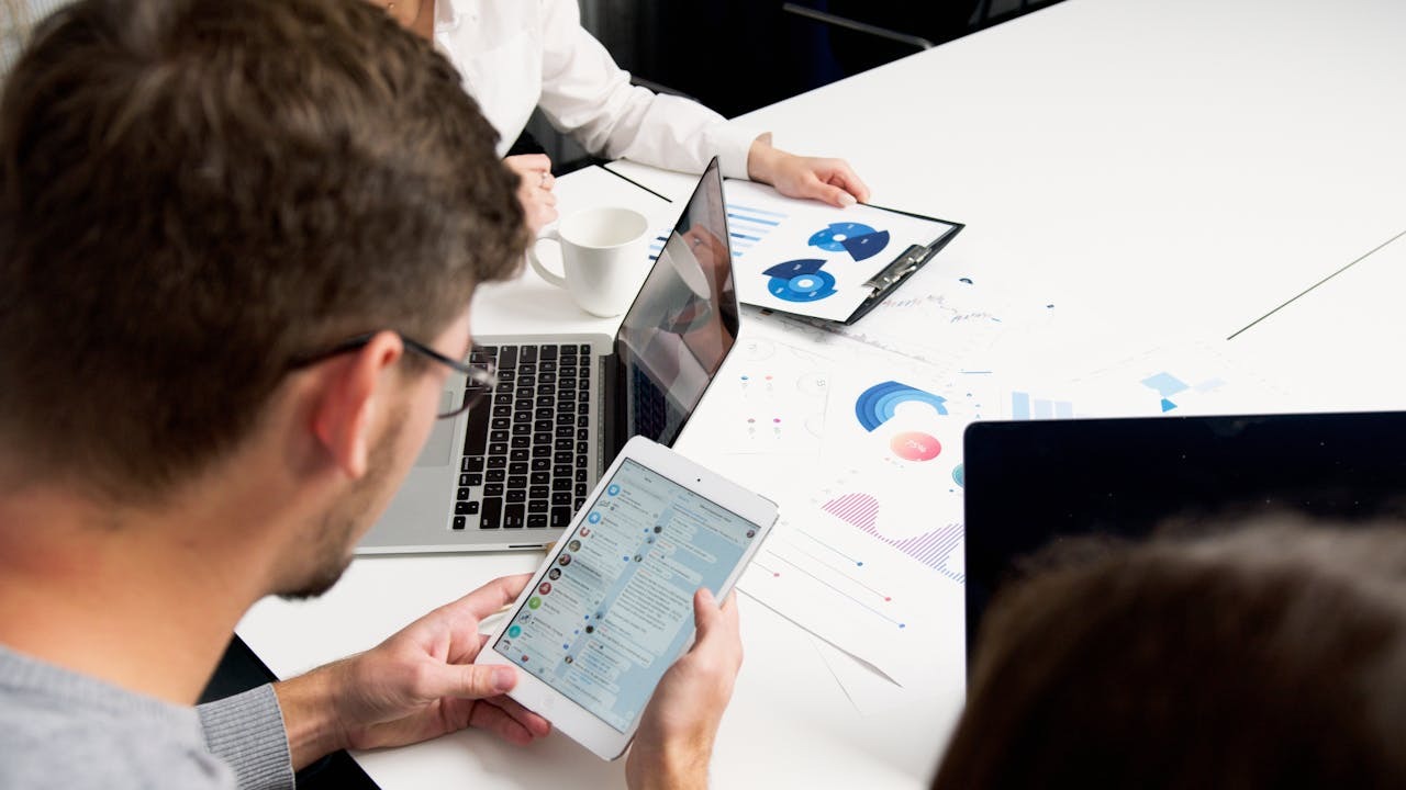 A professional using a tablet to manage communications and workflows while reviewing scheduling data analytics on a laptop.