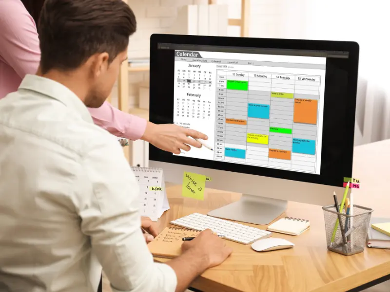 online scheduling platform multiuser calendar interface on desktop screen with colored event blocks and users pointing