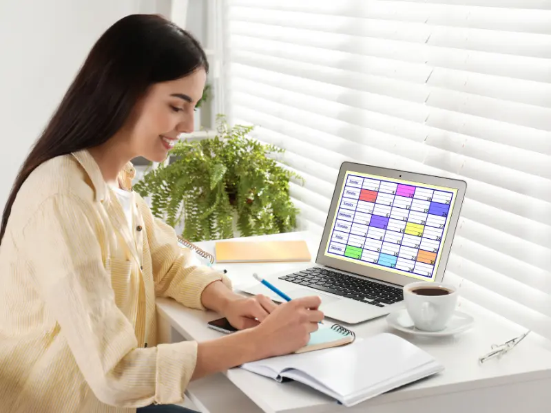 scheduling software vibrant calendar grid shown on laptop screen beside a user writing notes
