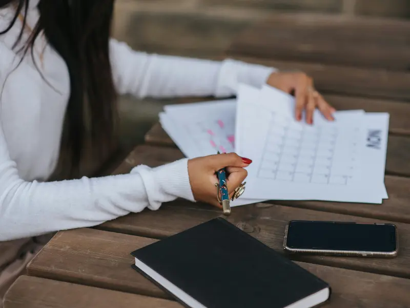 Customizable scheduling platform with a woman reviewing printed calendar sheets and making notes outdoors.