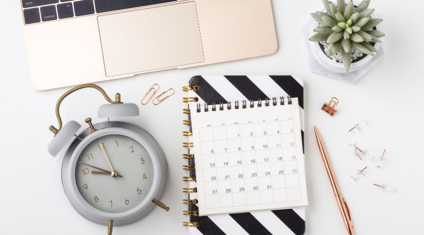 Flat lay of an alarm clock, calendar notepad and laptop
