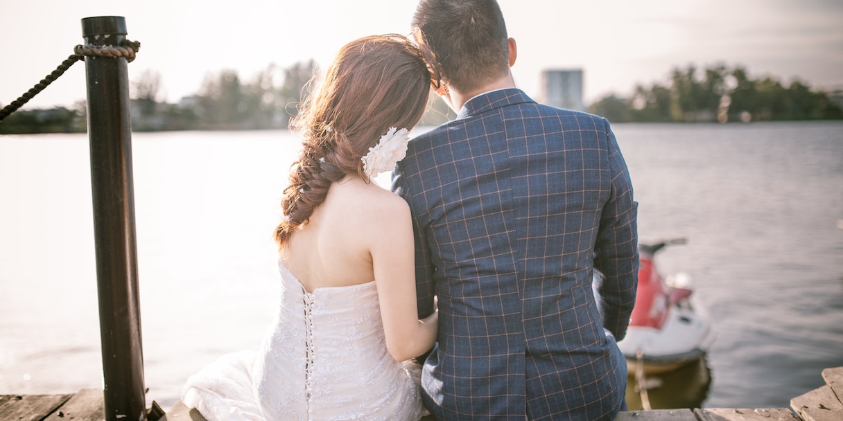 Bride and groom sitting by the water at sunset